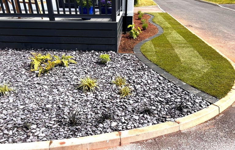 Newly laid striped lawn with block-edged border and slate-mulched planting bed by PC Landscaping in South Devon