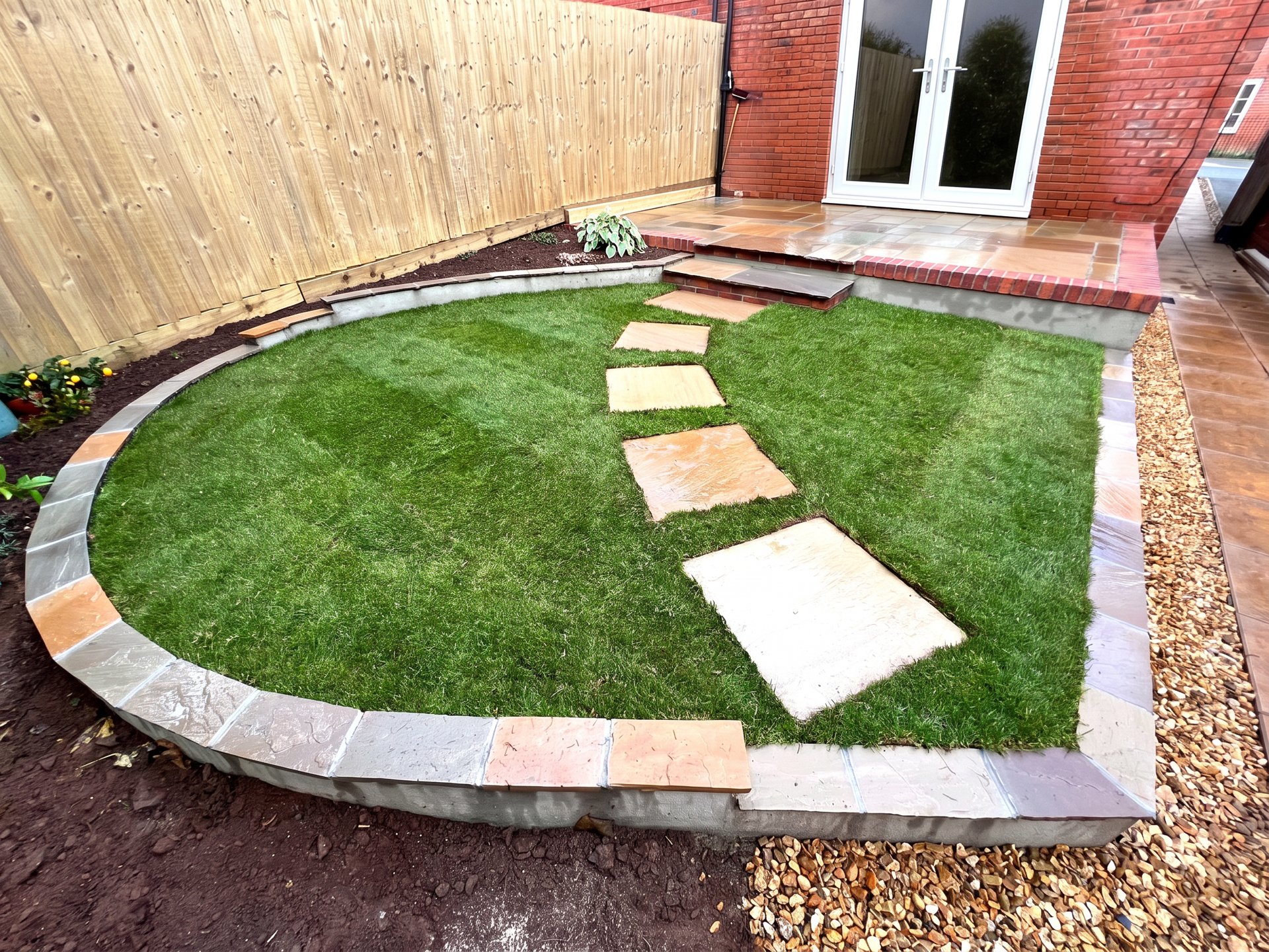 Sandstone patio with brick-edged steps, stepping-stone path and curved raised lawn built by PC Landscaping in South Devon