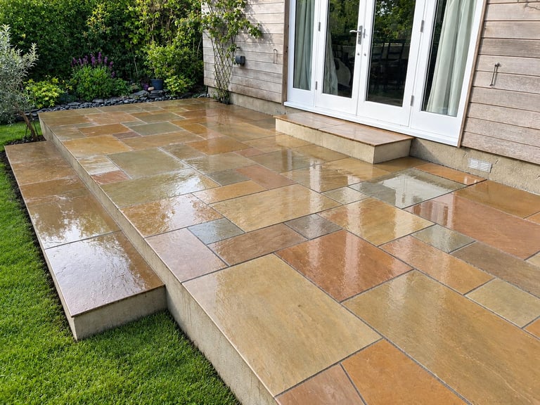 Indian sandstone patio with a raised step down to the lawn, laid by PC Landscaping outside a timber-clad home in South Devon